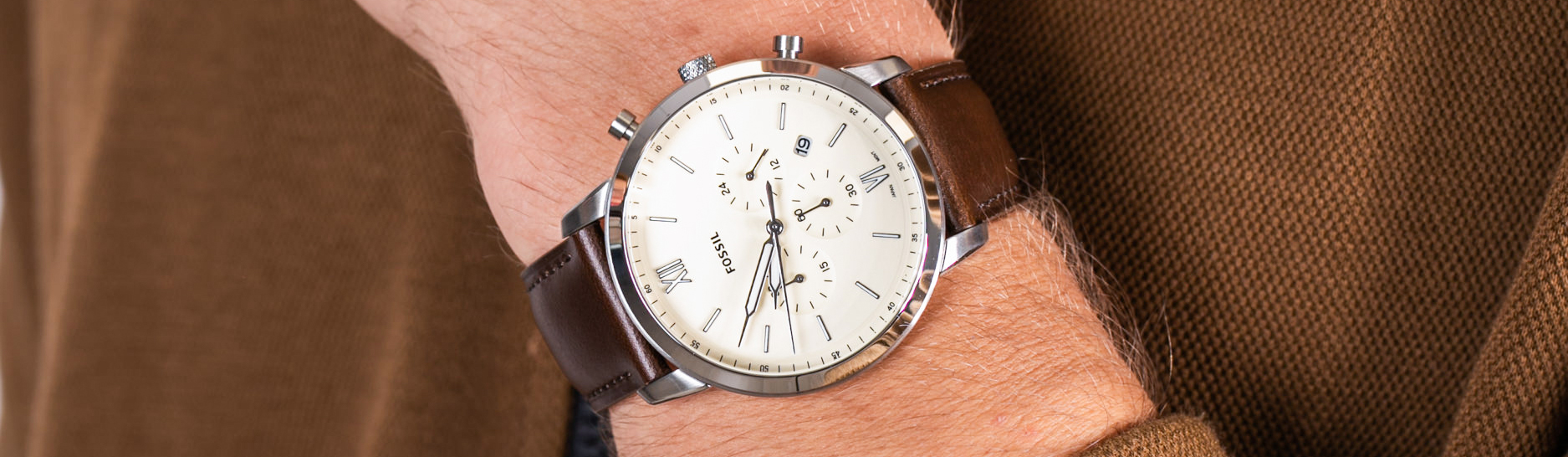 Chronograf Fossil z kremową tarczą na brązowym skórzanym pasku na nadgarstku mężczyzny, rękaw brązowej kurtki z zamkiem