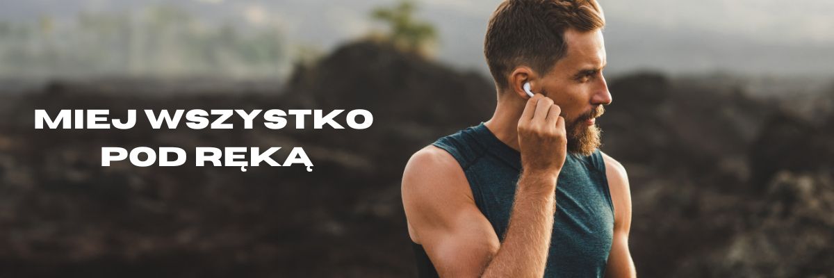 Mężczyzna w sportowym ubraniu dotyka bezprzewodowej słuchawki, w tle kamieniste pole.
