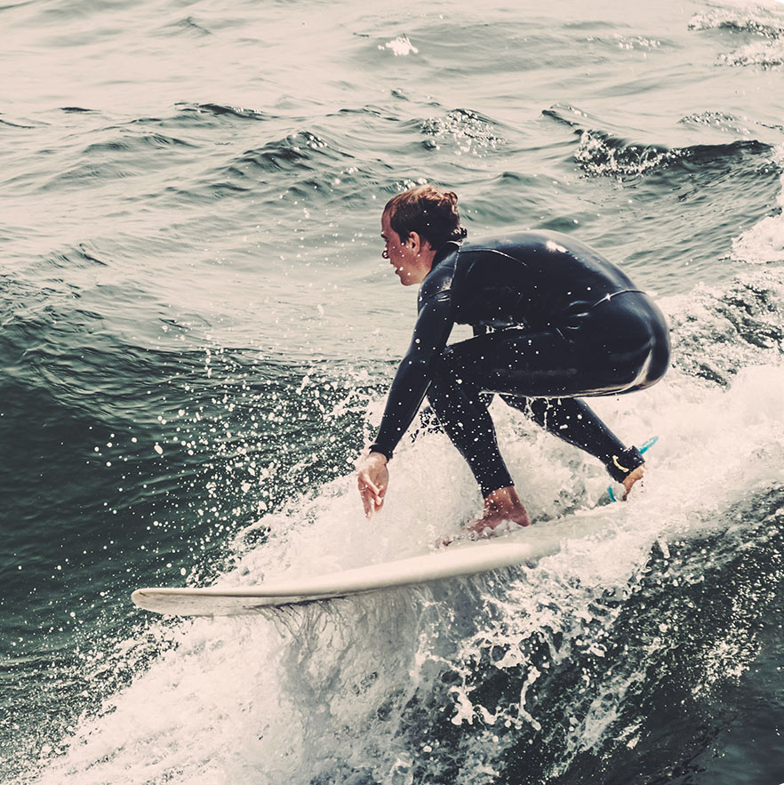 Surfer w neoprenie ślizga się po fali na desce surfingowej na morzu.