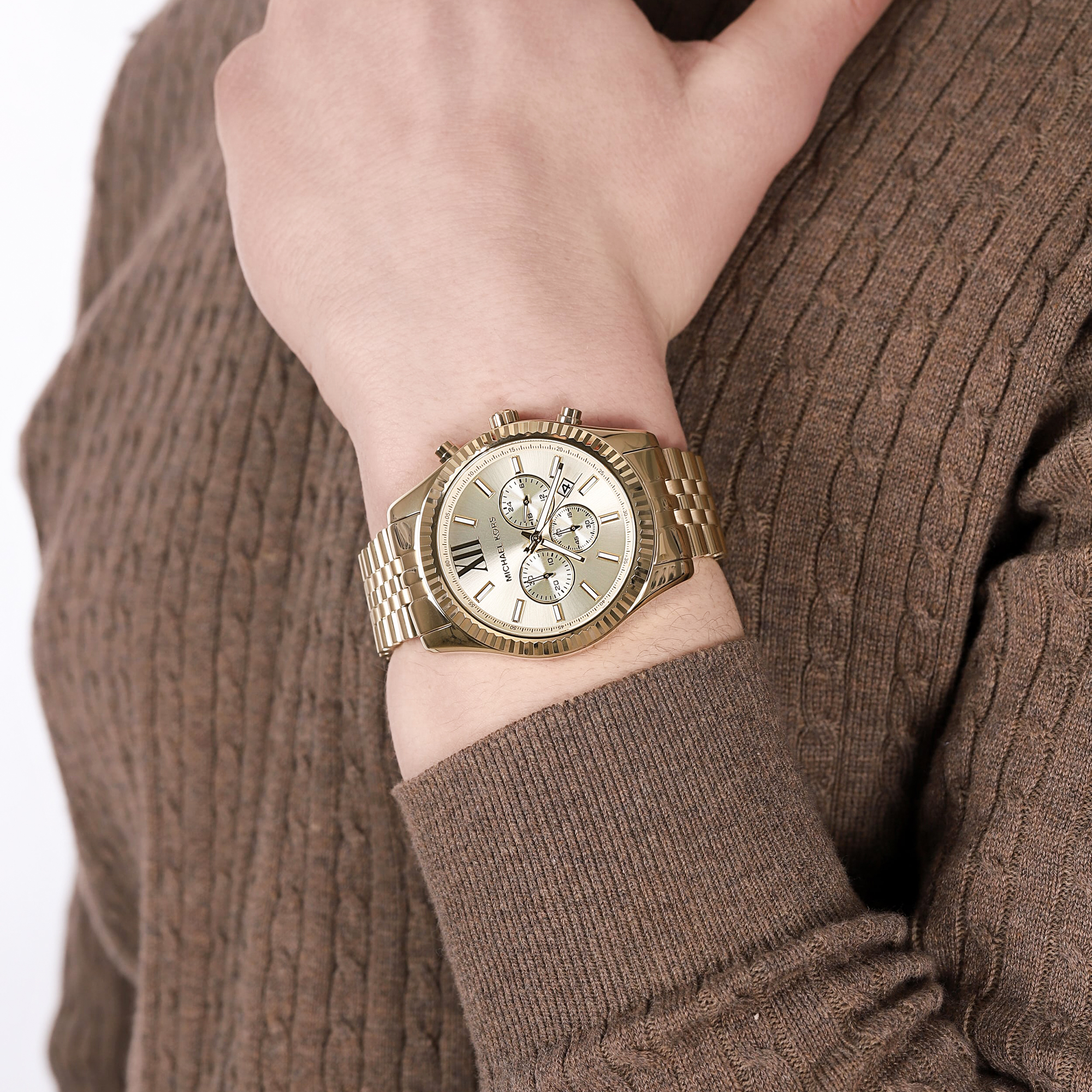 Złocony Michael Kors Lexington MK8281 z chronografem i ryflowaną lunetą na bransolecie na nadgarstku, rękaw brązowego swetra