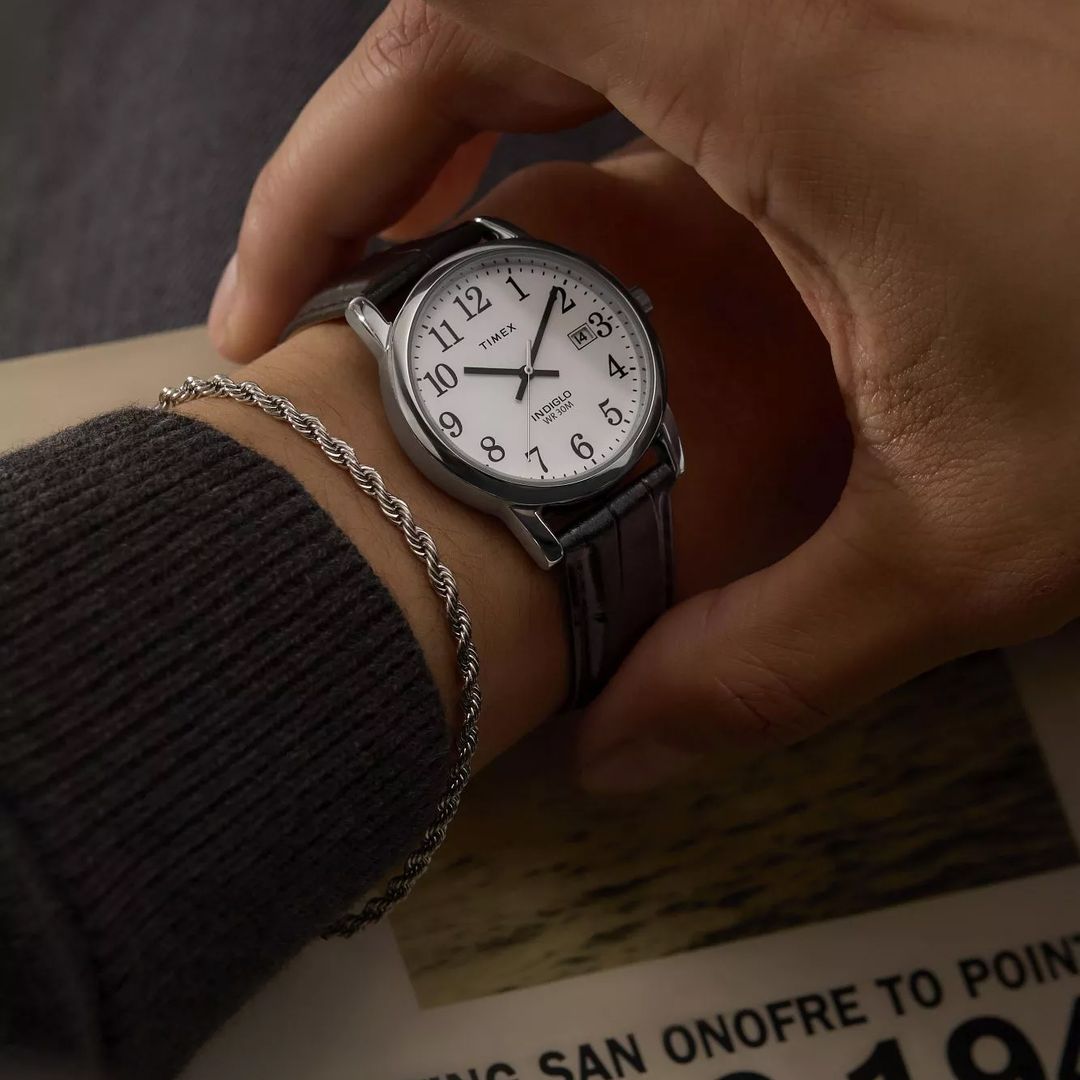 Zbliżenie na ręku na zegarek Timex z białą tarczą i czarnym paskiem imitującym skórę krokodyla