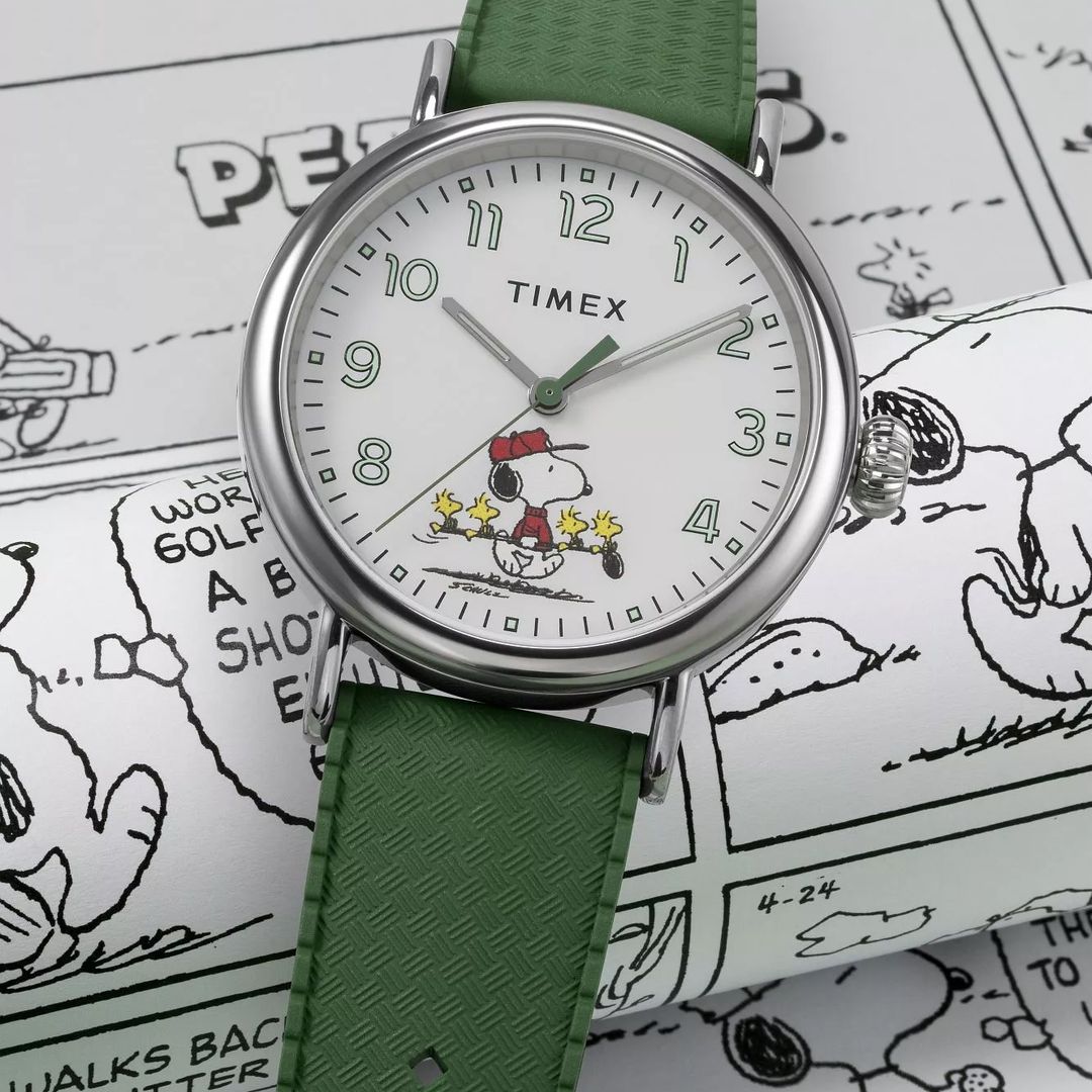 Zegarek Timex z białą tarczą, jasnymi cyframi arabskimi oraz Snoopy'm na dole tarczy
