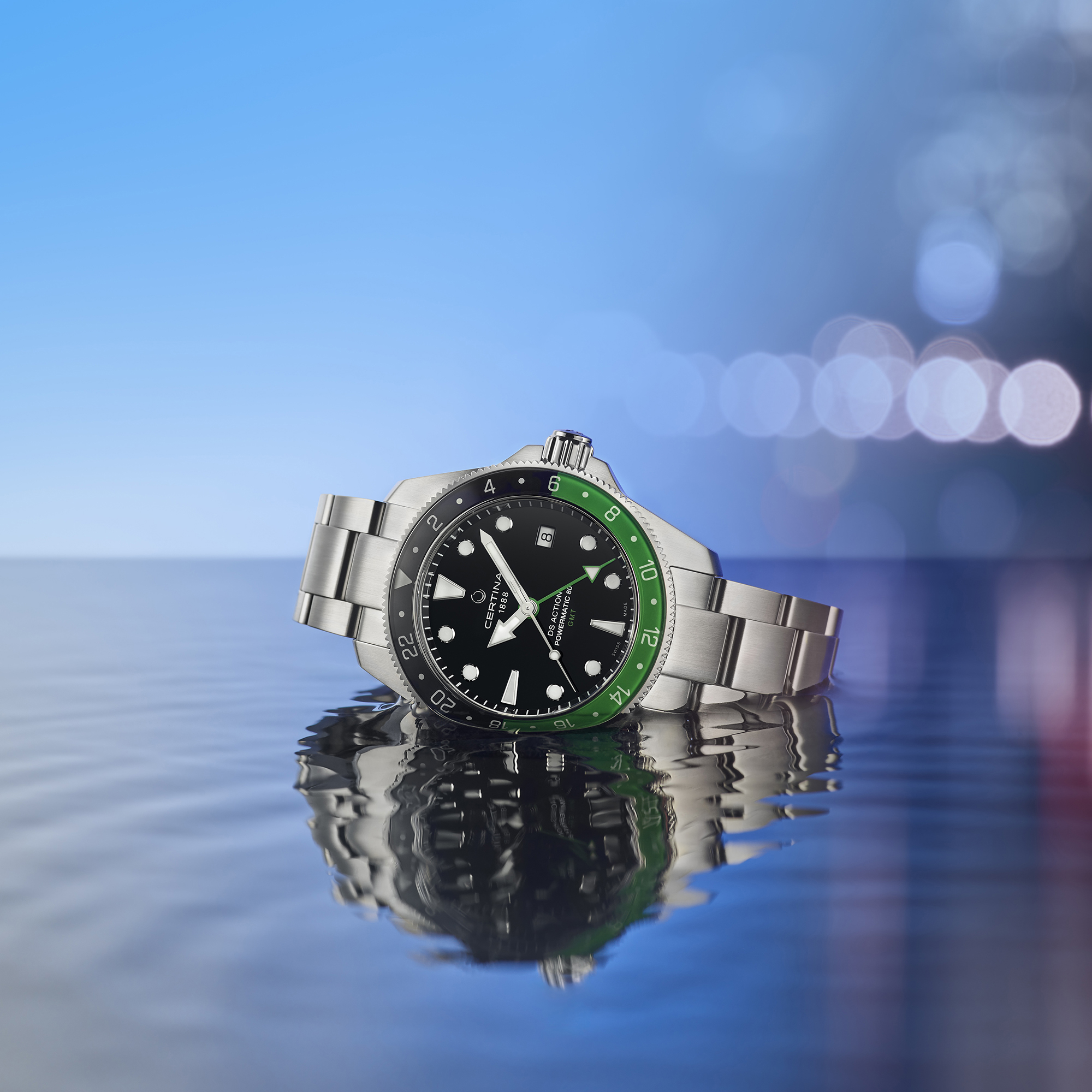 Diver Certina DS Action GMT Powermatic 80 na stalowej bransolecie leży na tafli wody, w tle niebo i światła