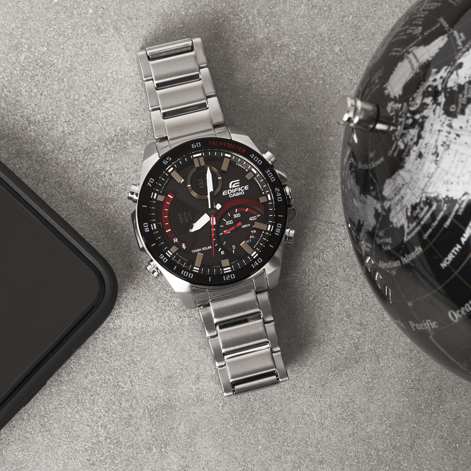 Srebrny zegarek Casio Bluetooth obok globusu na szarym tle