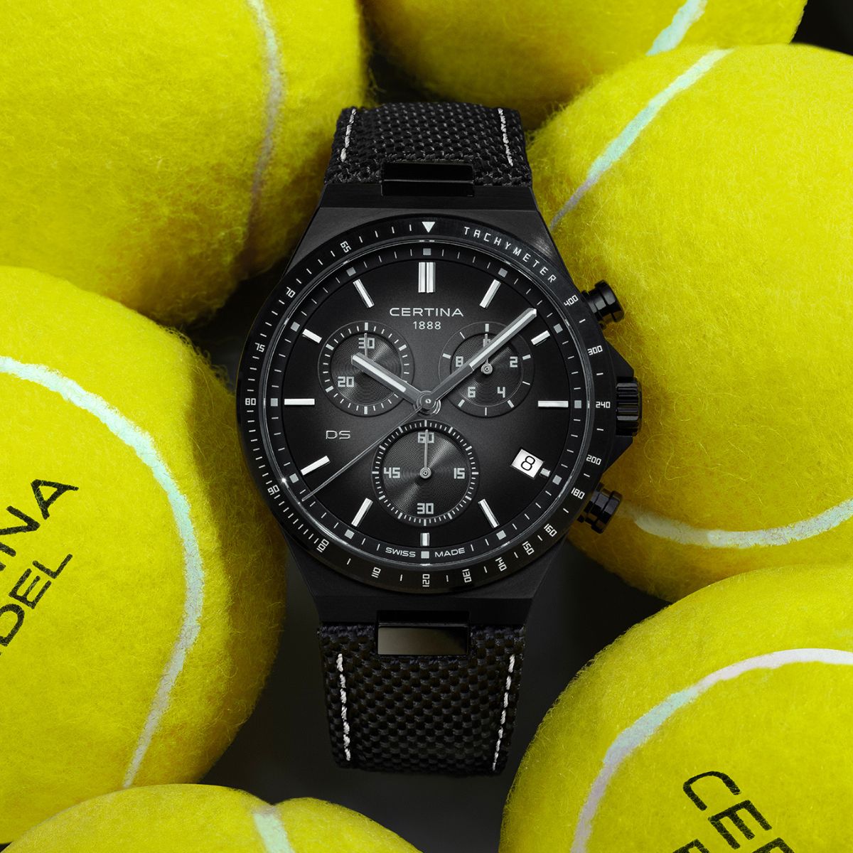 Czarny zegarek Certina Chronograph leżący pomiędzy piłkami tenisowymi