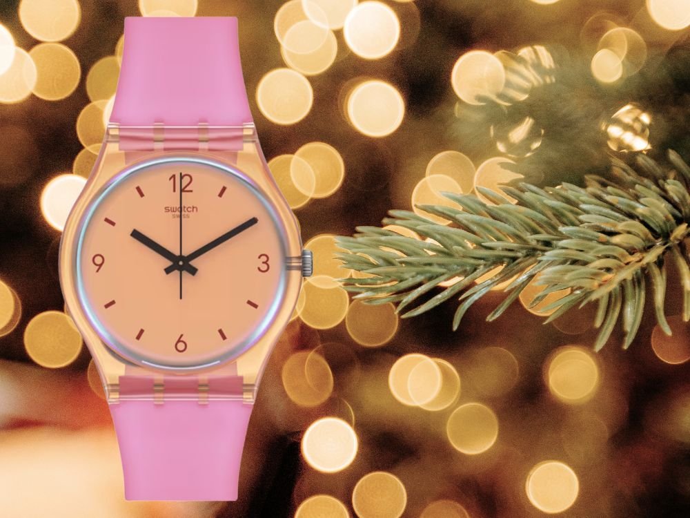 zegarek Swatch z różowym paskiem i pomarańczową tarczą na tle świątecznych lampek